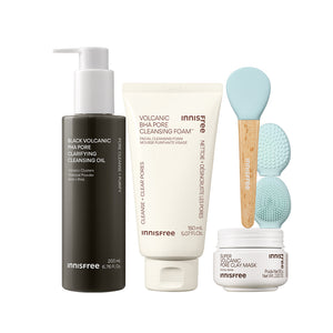 The Volcanic Pore Care Routine featuring Black Volcanic PHA Pore Cleansing Oil, Volcanic BHA Pore Cleansing Foam, two light blue silicone cleansing brushes with wooden handles, and a Super Volcanic Pore Clay Mask jar, all on a white background.