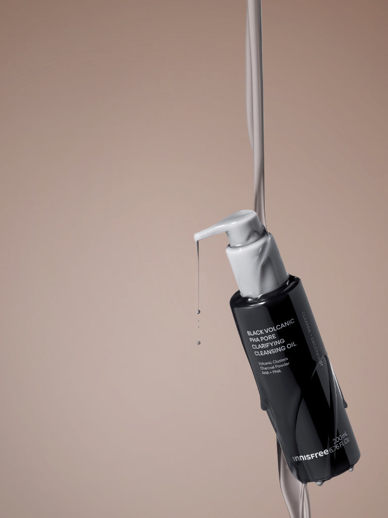 Innisfree Black Volcanic PHA Pore Clarifying Cleansing Oil suspended against a solid beige background with a liquid stream dripping from the nozzle.