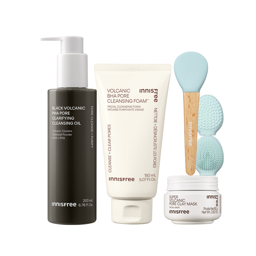 The Volcanic Pore Care Routine featuring Black Volcanic PHA Pore Cleansing Oil, Volcanic BHA Pore Cleansing Foam, two light blue silicone cleansing brushes with wooden handles, and a Super Volcanic Pore Clay Mask jar, all on a white background.