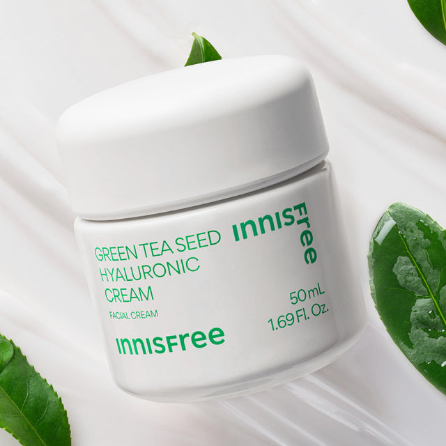 Innisfree Green Tea Seed Hyaluronic Cream in a white 50 mL jar, styled with green tea leaves on a white background with cream swirls.