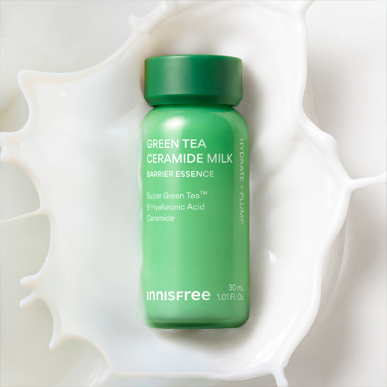 A green mini Innisfree Green Tea Ceramide Milk barrier essence bottle, styled on a white milk splash background.