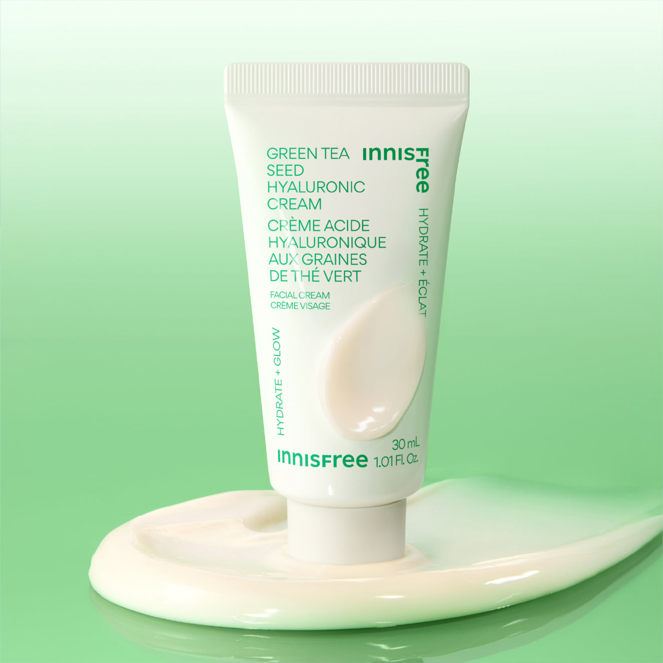 Mini Innisfree Green Tea Seed Hyaluronic Cream in a white squeeze tube, styled on top of a thick, glossy smear of the white cream against a soft green gradient background.