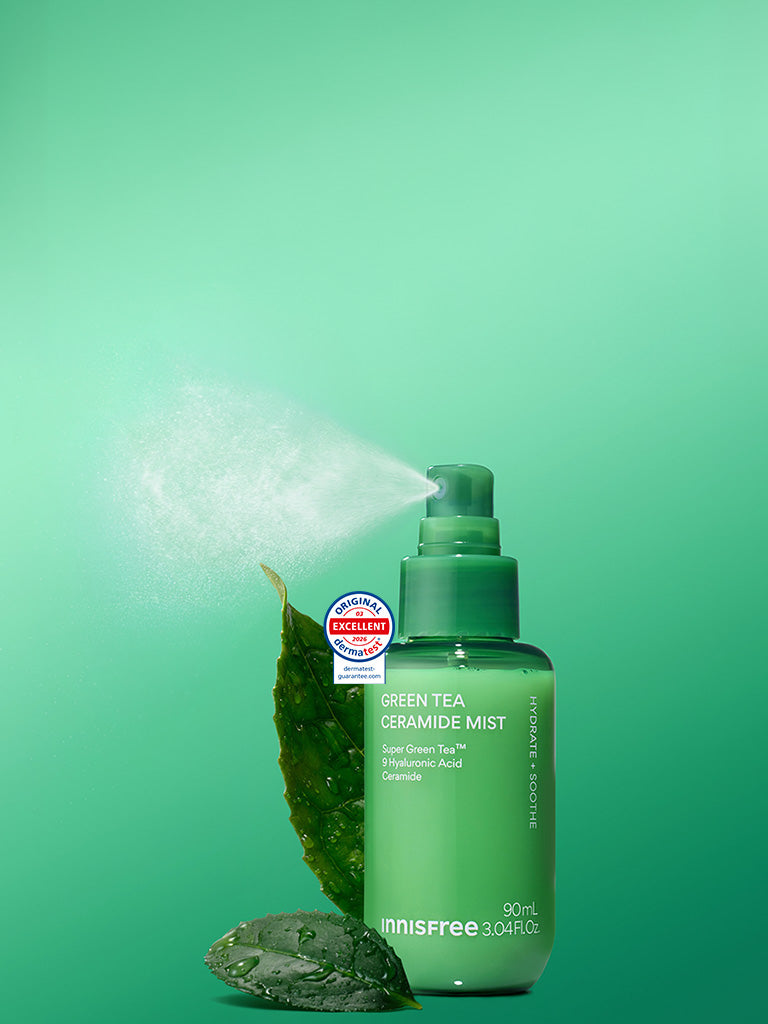 Green Tea Ceramide Mist with a leaf and stone prop, shown on a bright green gradient background with mist coming from the sprayer.