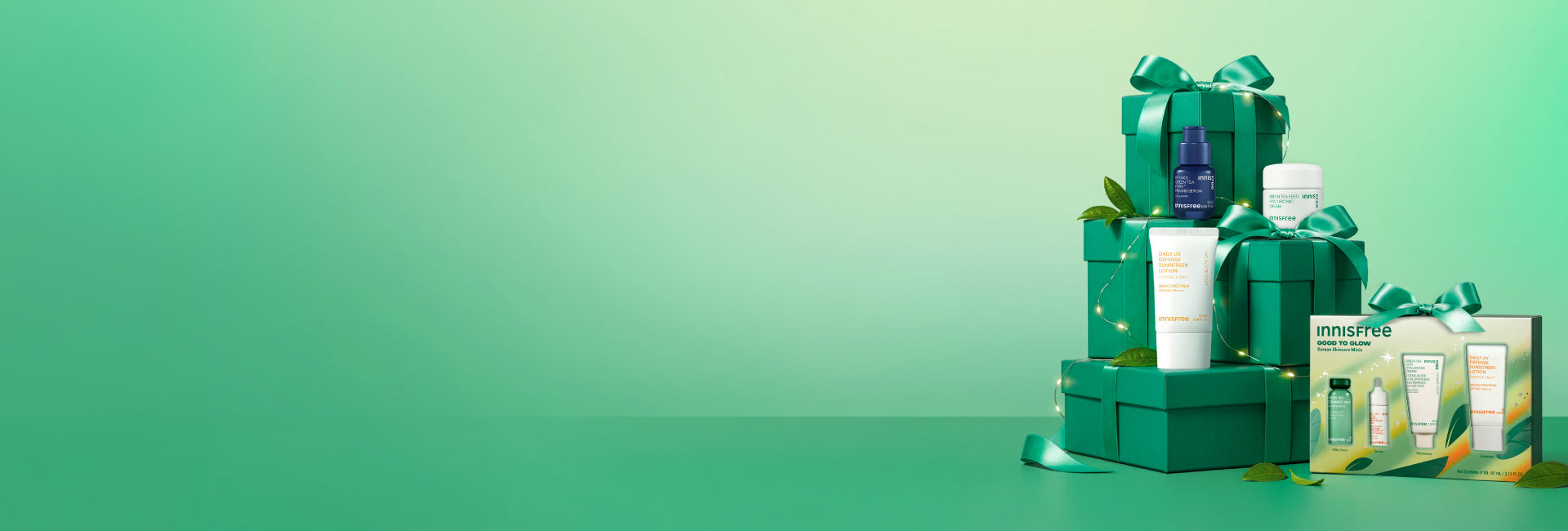 Innisfree Good to Glow Set and Green Tea PDRN™ Serum, Green Tea Hyaluronic Cream, and a Daily UV Defense Sunscreen SPF 50+ arranged on a stack of green gift boxes with ribbons against a mint green gradient background.