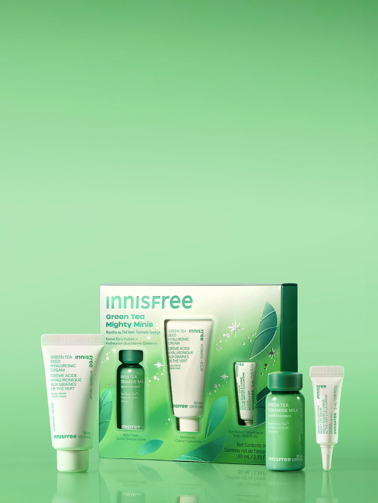 Green Tea Mighty Minis set with skincare tubes and bottles in white and green packaging, displayed on a reflective green surface against a light green gradient background.