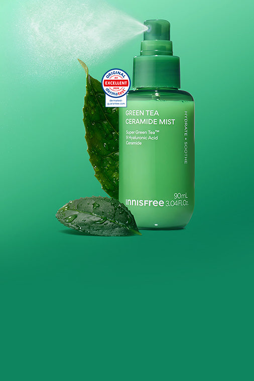 Green Tea Ceramide Mist with a leaf and stone prop, shown on a bright green gradient background with mist coming from the sprayer.