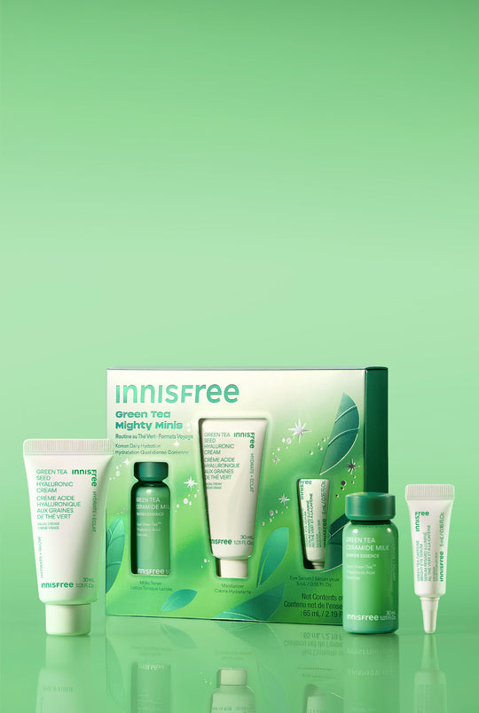 Green Tea Mighty Minis set with skincare tubes and bottles in white and green packaging, displayed on a reflective green surface against a light green gradient background.