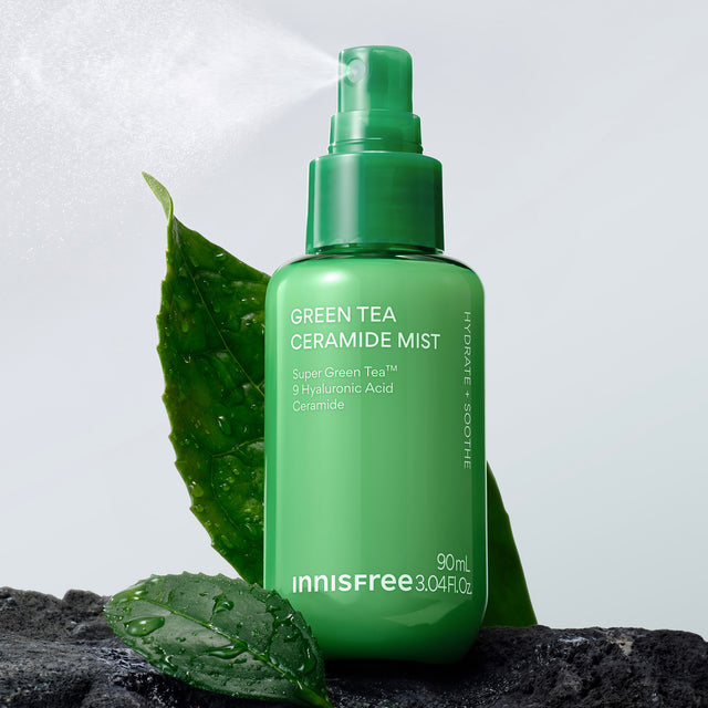 Innisfree Green Tea Ceramide Mist  shown spraying with mist visible in the air, styled with green leaves on a dark rock against a light gray background.