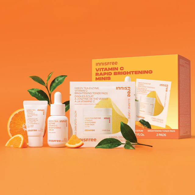 Innisfree Vitamin C Rapid Brightening Minis skincare set arranged on a bright orange background styled with orange slices and green leaves.