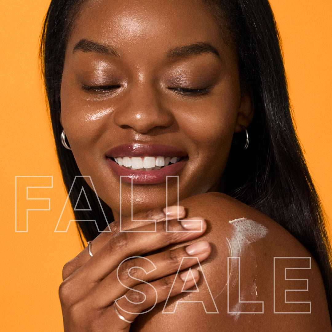 A close-up lifestyle shot of a woman with closed eyes, smiling, with her hand on her shoulder applying Daily UV Sunscreen SPF 50+. She is wearing hoop earrings against a solid orange background, with a 'FALL SALE' text overlay.