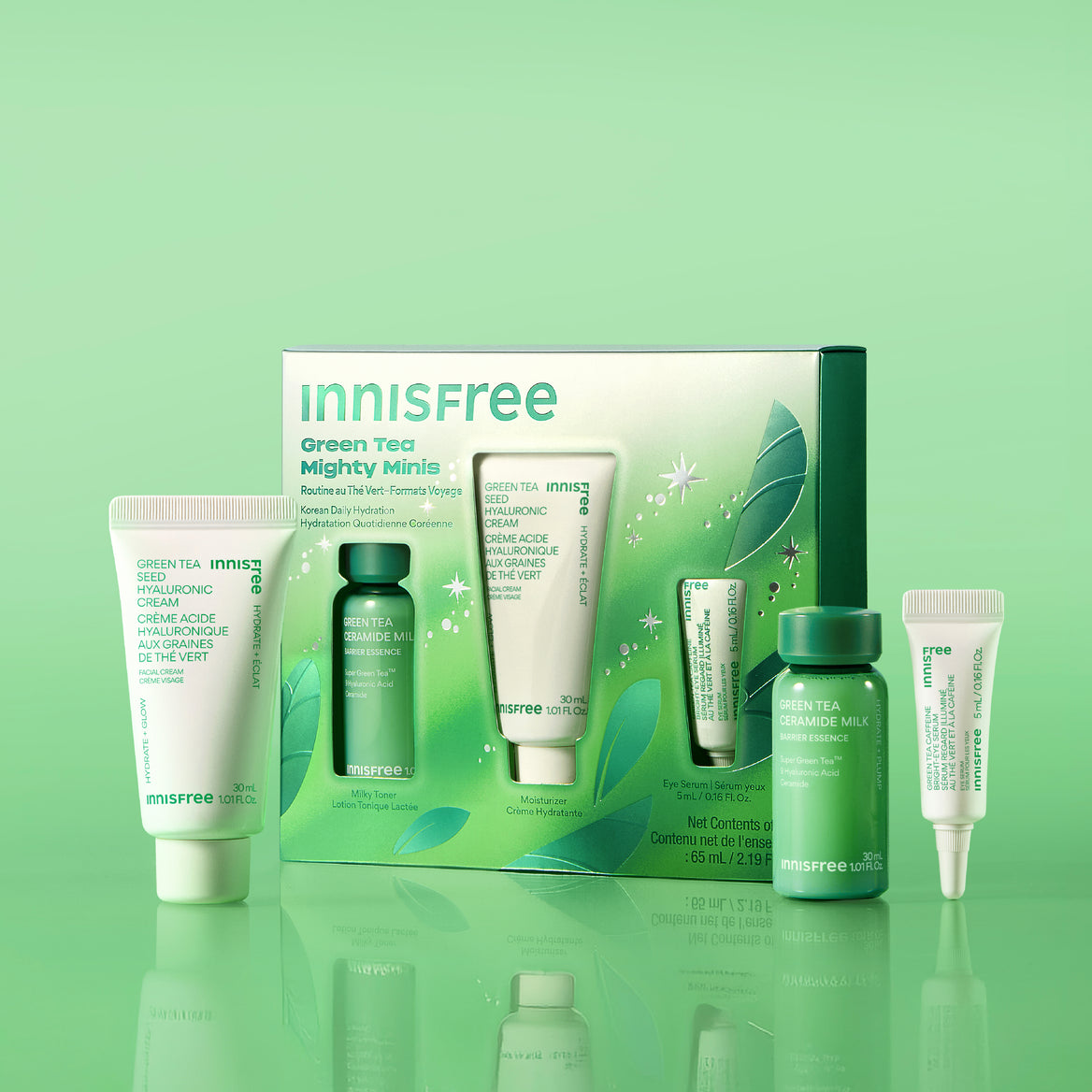 Green Tea Mighty Minis set with skincare tubes and bottles in white and green packaging, displayed on a reflective green surface against a light green gradient background.