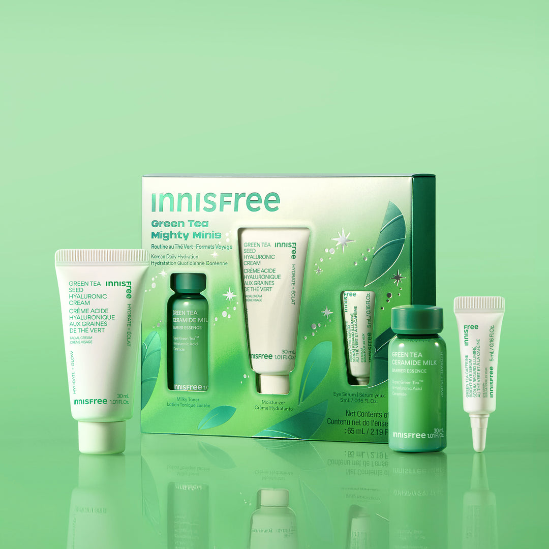 Green Tea Mighty Minis set with skincare tubes and bottles in white and green packaging, displayed on a reflective green surface against a light green gradient background.