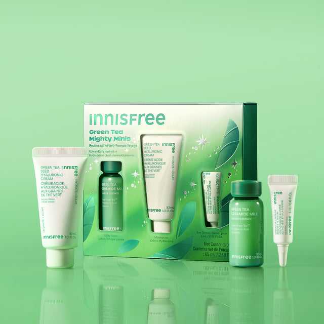 Green Tea Mighty Minis set with skincare tubes and bottles in white and green packaging, displayed on a reflective green surface against a light green gradient background.