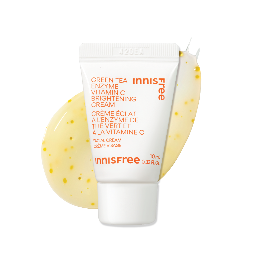 Innisfree Green Tea Enzyme Vitamin C Brightening Cream in a white squeeze tube with orange text, set against a white background with a yellow cream smear behind it.