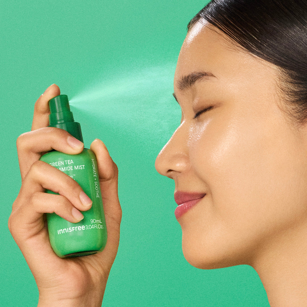 A woman in profile holds a green Innisfree Green Tea Mist to her face against a solid green background.